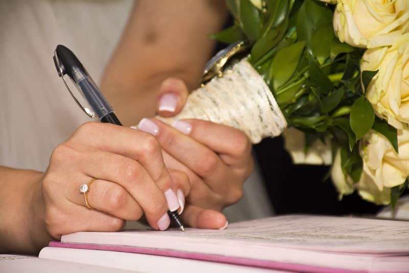 Bride holding a bouquet of flowers and signing a prenup to illustrate our article on the benefits of prenuptial agreements in Georgia.